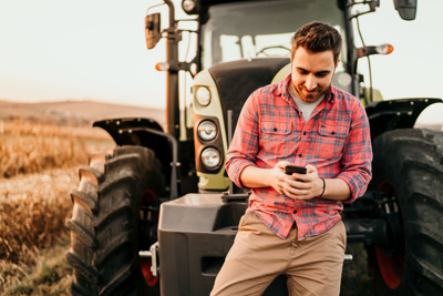 Bauer vor Traktor mit dem Smartphone